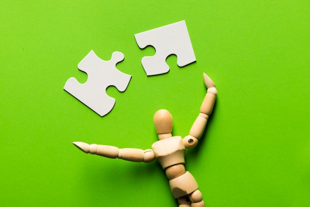Pezzo di puzzle con figura umana in legno su sfondo verde