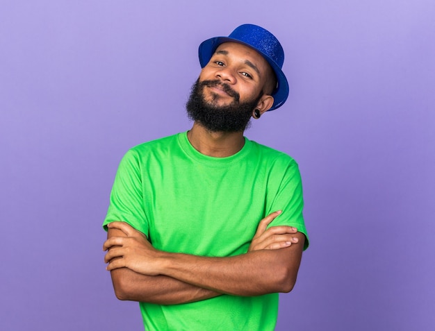 Piacere guardando fotocamera giovane ragazzo afro-americano che indossa un cappello da festa incrociando le mani