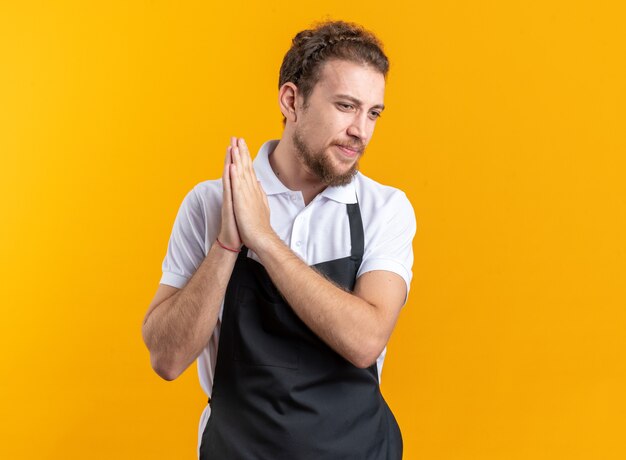 Piacere guardando lato giovane barbiere maschio che indossa l'uniforme tenendosi per mano insieme isolato sul muro giallo