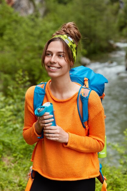 Piacevole giovane turista femminile ha un'escursione notevole, gode di una bevanda calda, tiene la fiaschetta