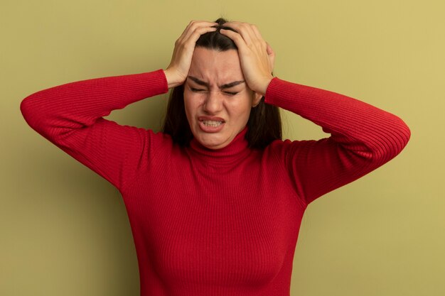 Piangere la donna abbastanza caucasica le mani sulla testa su verde oliva