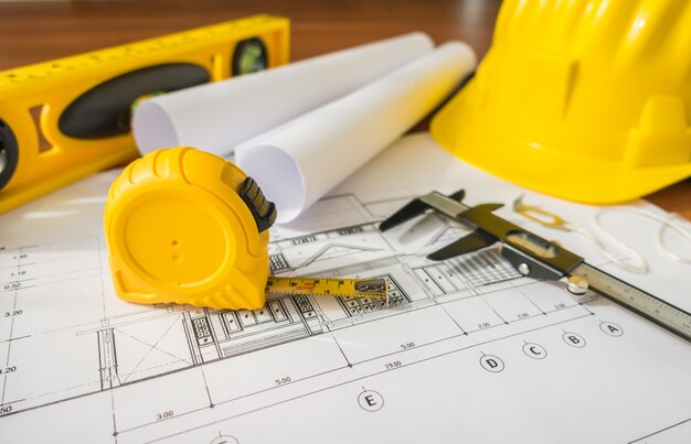 Piani di costruzione con il casco giallo e strumenti di disegno su Bluep