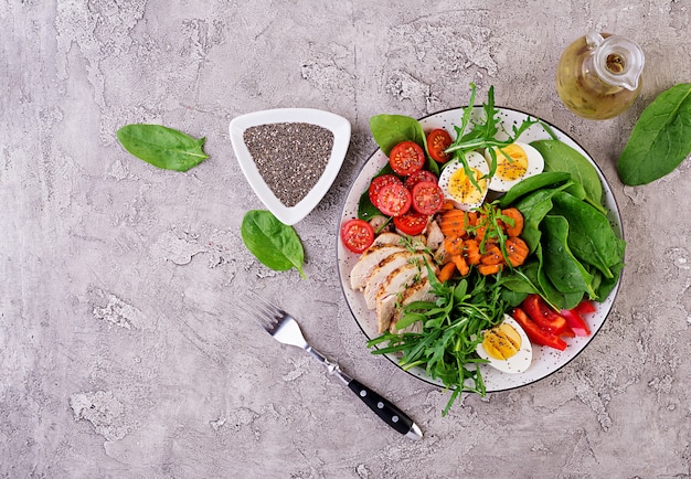 Piastra con un alimento dieta cheto. Pomodorini, petto di pollo, uova, carota, insalata con rucola e spinaci. Pranzo di Keto. Vista dall'alto