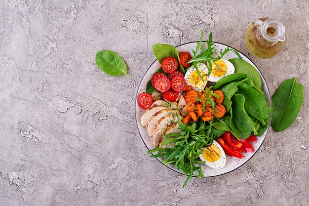 Piastra con un alimento dieta cheto. Pomodorini, petto di pollo, uova, carota, insalata con rucola e spinaci. Pranzo di Keto. Vista dall'alto