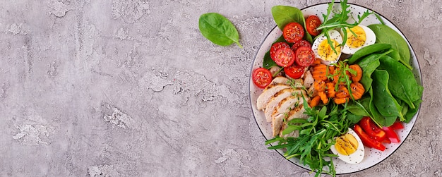 Piastra con un alimento dieta cheto. Pomodorini, petto di pollo, uova, carota, insalata con rucola e spinaci. Pranzo di Keto. Vista dall'alto