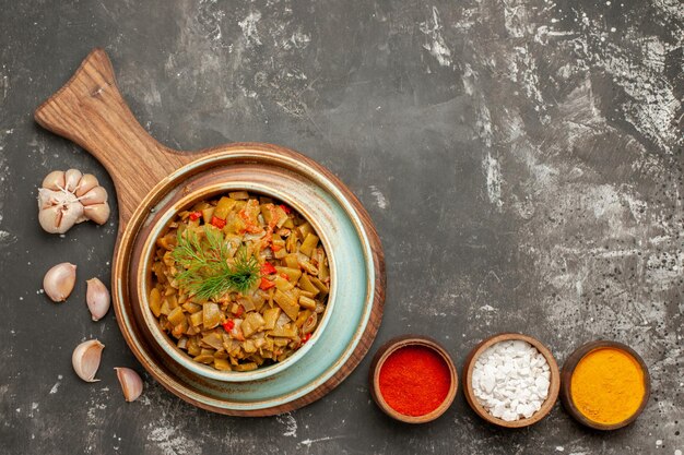 piatto appetitoso tre spezie aglio accanto agli appetitosi fagiolini e pomodori sul tagliere sul tavolo nero