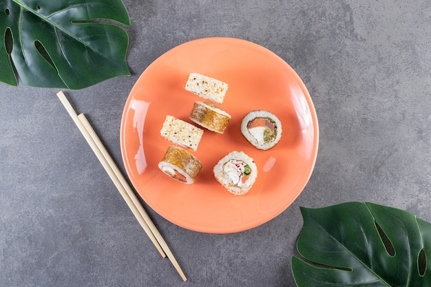 Piatto arancione di involtini di sushi con tonno su sfondo di pietra.