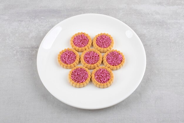 Piatto bianco di biscotti dolci con granelli rosa sul tavolo di pietra.