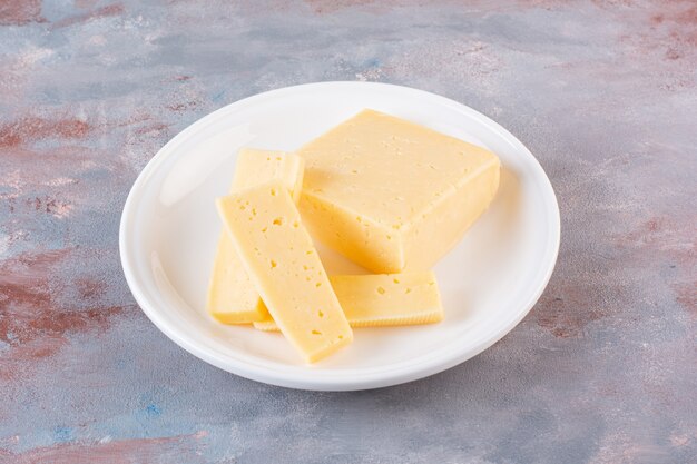 Piatto bianco di fette di formaggio giallo sulla superficie di marmo.