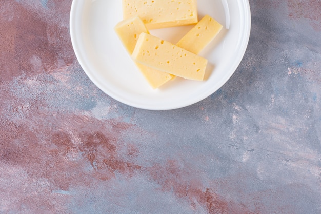 Piatto bianco di fette di formaggio giallo sulla superficie di marmo.
