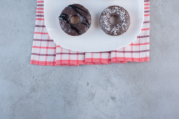 Piatto bianco di gustose ciambelle al cioccolato su pietra.