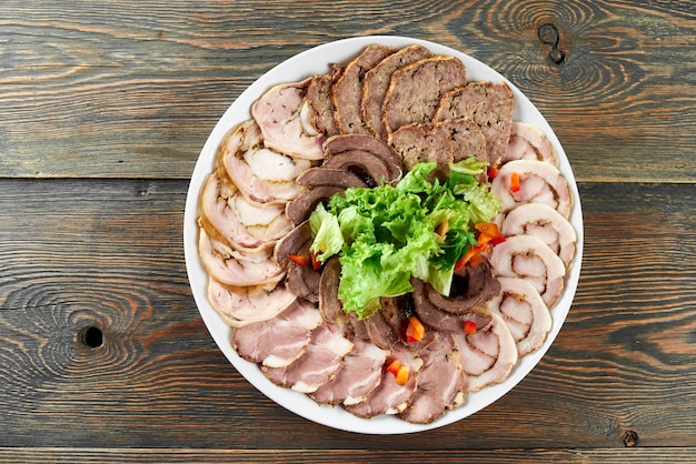 Piatto bianco su un tavolo di legno pieno di fette di carne ripiene, decorato con foglie di lattuga fresca e pezzi di paprika.