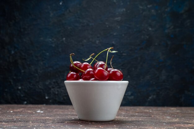 Piatto bianco vista frontale con ciliege fresche rosse aspre sullo scrittorio di legno marrone