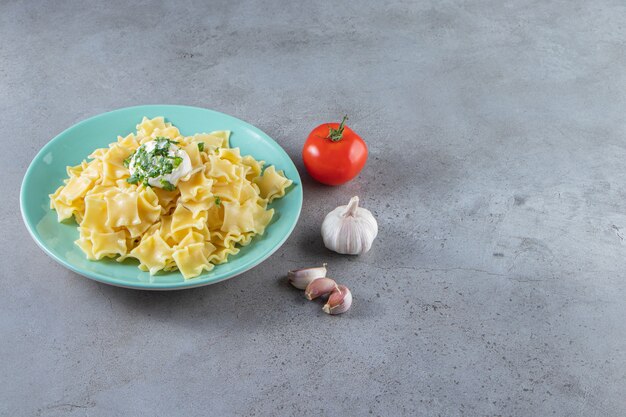 Piatto blu di pasta bollita deliziosa su fondo di pietra.