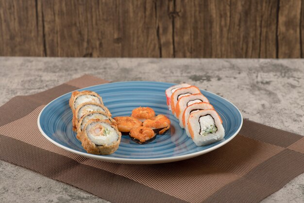 Piatto blu di vari rotoli di sushi sul tavolo di marmo