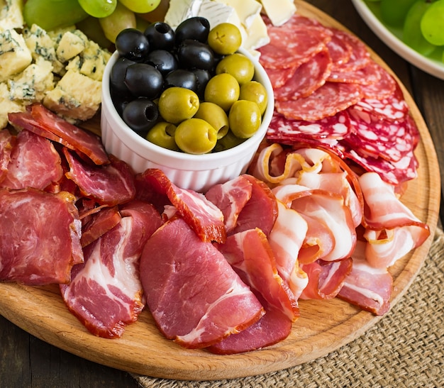 Piatto di antipasto con pancetta, scatti, salame, formaggio e uva su un tavolo di legno