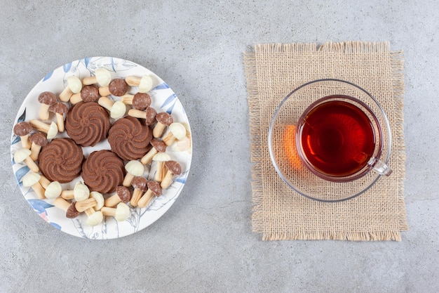 Piatto di biscotti con funghi al cioccolato accanto a una tazza di tè su sfondo marmo. Foto di alta qualità