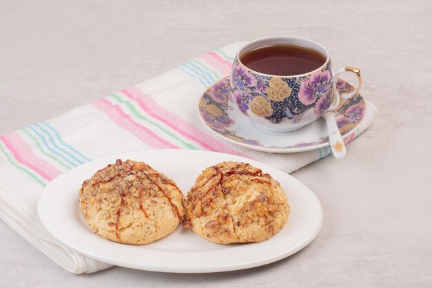 Piatto di biscotti e tazza di tè sul tavolo bianco.