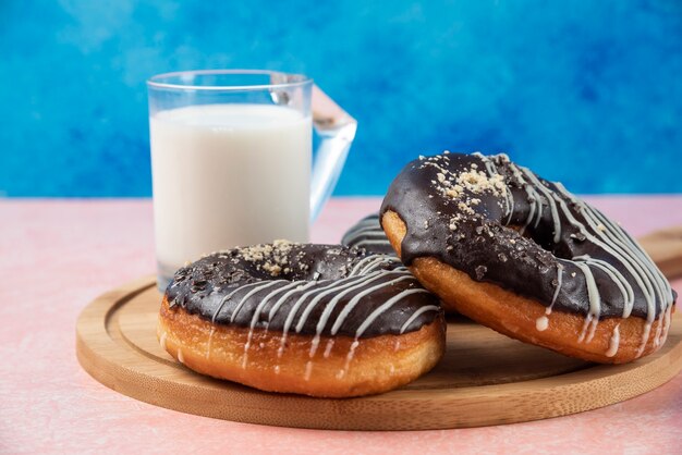 Piatto di ciambelle al cioccolato con un bicchiere di latte sul tavolo rosa.