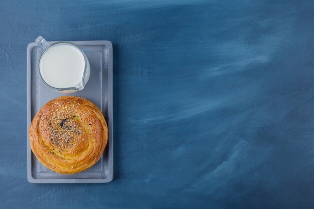 Piatto di deliziosa pasticceria con semi neri e bicchiere di latte sulla superficie blu.