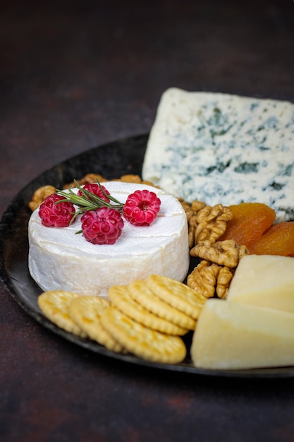 Piatto di formaggi su oscurità con formaggio camembert, gorgonzola, gauda e bacche e snack