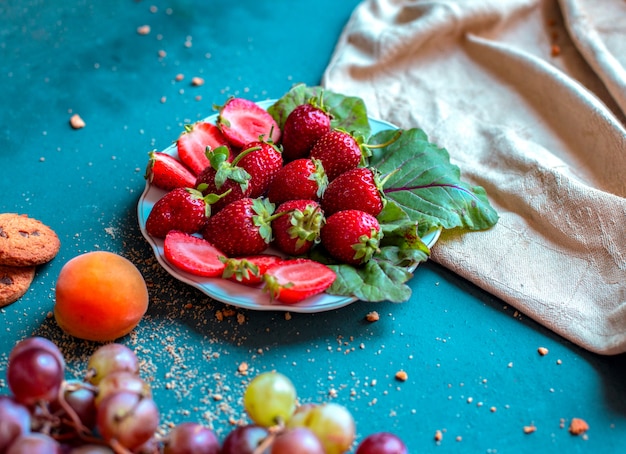 Piatto di fragole con frutti misti intorno su un tavolo blu.