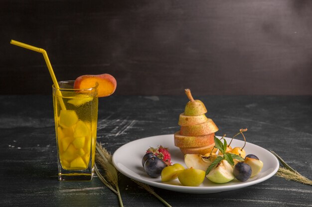 Piatto di frutta bianca isolato sulla parete nera con un bicchiere di succo