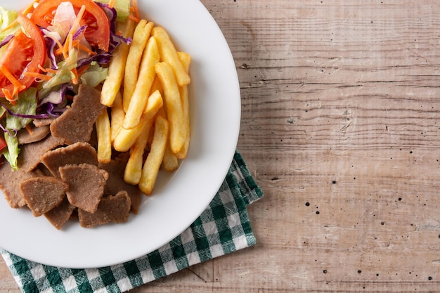 Piatto di kebab, verdure e patatine fritte sulla tavola di legno