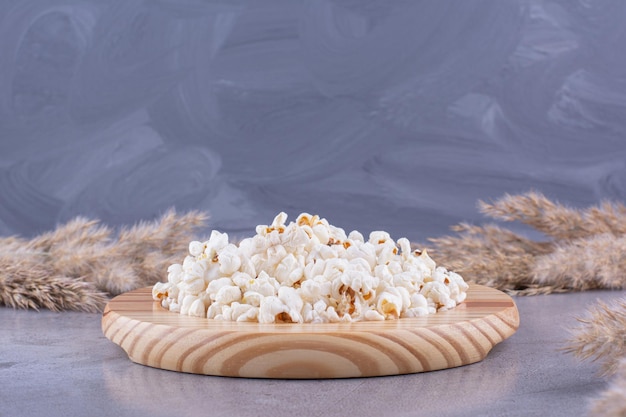 Piatto di legno con una porzione di popcorn posta nel mezzo di aghi essiccati su fondo marmo. Foto di alta qualità