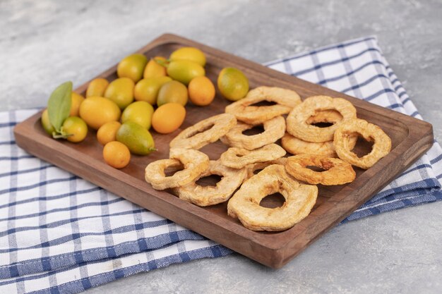 Piatto di legno di cumquat freschi e anelli di mela essiccati su fondo di marmo.