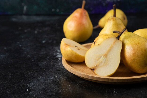 Piatto di legno di deliziose pere gialle sulla superficie nera.