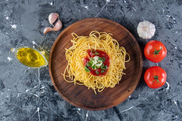 Piatto di legno di deliziosi spaghetti con salsa di pomodoro e verdure sulla superficie in marmo.