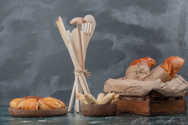Piatto di legno di panetteria con utensili da cucina su sfondo marmo.