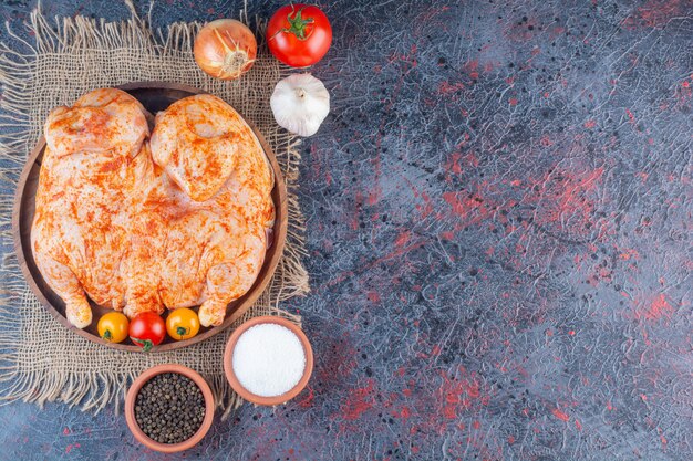 Piatto di legno di pollo intero marinato sulla superficie di marmo.