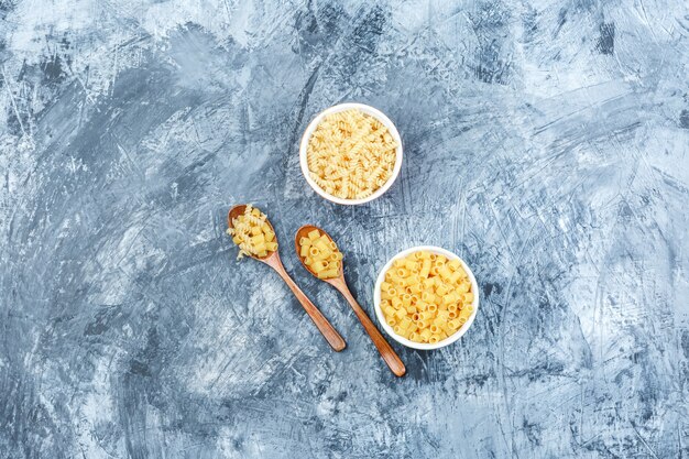 Piatto di pasta cruda laici in ciotole e cucchiai di legno su una schifezza sullo sfondo di gesso. orizzontale