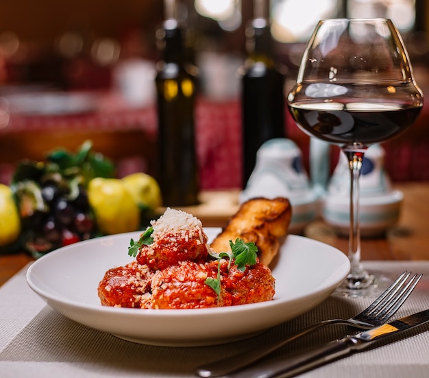 Piatto di polpette guarnito con salsa di pomodoro grattugiato parmigiano e prezzemolo servito con vino rosso