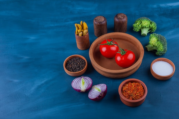 Piatto di pomodori freschi, cipolla, broccoli e condimenti sulla superficie blu.