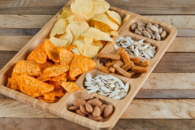 Piatto di snack assortiti su un tavolo di legno. Patatine, cracker, mandorle, pistacchi, semi di girasole.