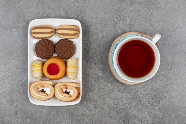 Piatto di vari dessert e tazza di tè su marmo.