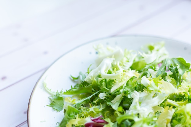 Piatto in ceramica bianca con insalata fresca su una superficie di legno