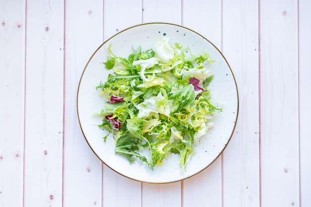 Piatto in ceramica bianca con insalata fresca su una superficie di legno