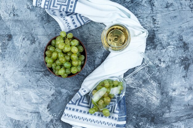 Piatto laici bicchiere di uva bianca con un bicchiere di whisky, ciotola di uva, carta da cucina su sfondo di marmo blu scuro. orizzontale