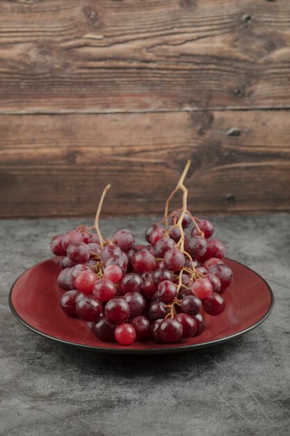 Piatto rosso di uva fresca posto sulla superficie in marmo.