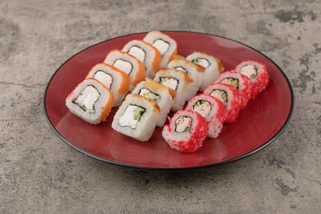 Piatto rosso di vari deliziosi involtini di sushi su fondo di marmo