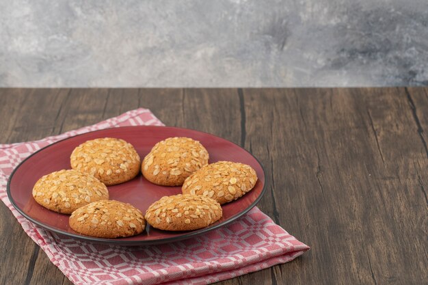 Piatto rosso pieno di biscotti di farina d'avena con semi e cereali posti sulla tavola di legno