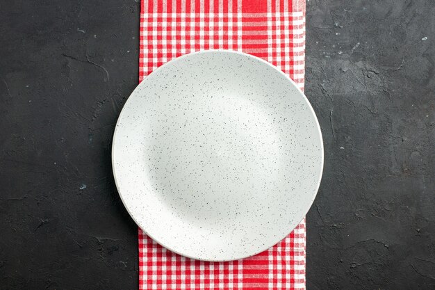 Piatto rotondo bianco di vista superiore sul tovagliolo a quadretti rosso e bianco sul posto scuro della copia del tavolo