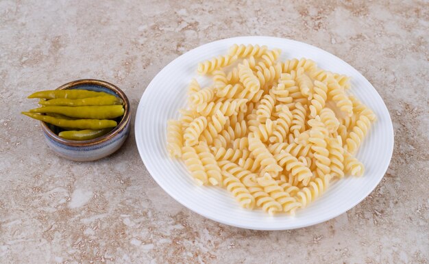 Piatto semplice di pasta e una piccola ciotola di peperoni sott'aceto sulla superficie di marmo.