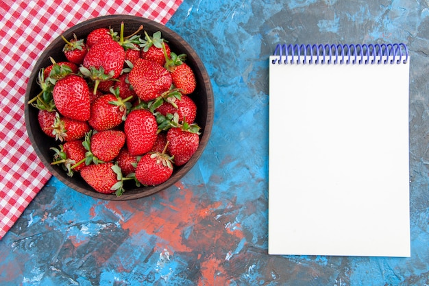 Piatto vista dall'alto con fragole fresche e gustose frutta matura con blocco note su sfondo blu