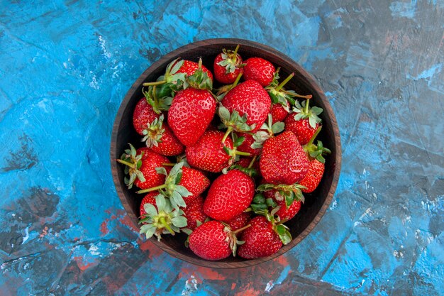 Piatto vista dall'alto con fragole fresche e gustose frutti maturi su sfondo blu