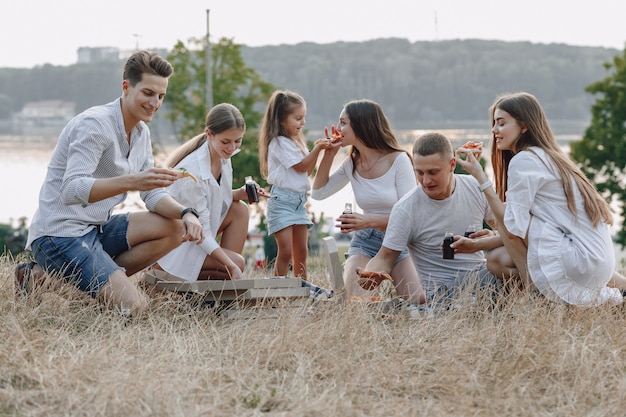 Pic-nic amici con pizza e bevande, giornata di sole, tramonto, compagnia, divertimento, coppie e mamma con bambino